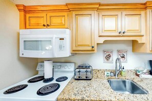 A kitchen with wooden cabinets, a white microwave, a stove with four burners, a toaster, and a stainless steel sink. - Bay Watch Resort 0534 (North Myrtle Beach)
