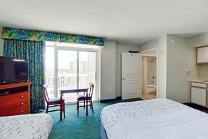 Ein Hotelzimmer mit Bett, Schreibtisch, Stuhl, Fernseher und einem Balkon mit Vorhängen.