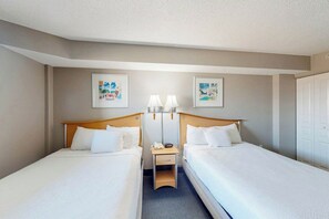 A hotel room with two single beds, a bedside table with a lamp, and artwork on the walls. - Bay Watch Resort 0606 (North Myrtle Beach)