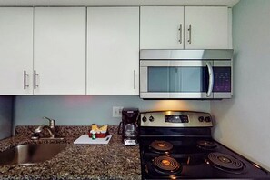 Eine Küche mit weißen Schränken, einem Edelstahlbackofen, einer Mikrowelle, einem Gasherd und einer Arbeitsplatte aus Granit.