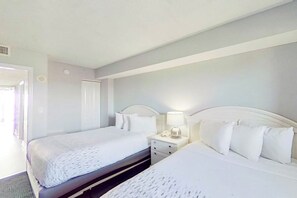 A hotel room with two beds, a bedside table with a lamp, and a door leading to another room. - Bay Watch Resort 0607 (North Myrtle Beach)