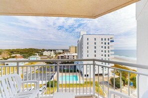 Un balcon avec vue sur une piscine, une plage et les bâtiments environnants.