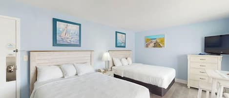 Habitación de hotel con dos camas, un escritorio, una televisión y obras de arte en las paredes.