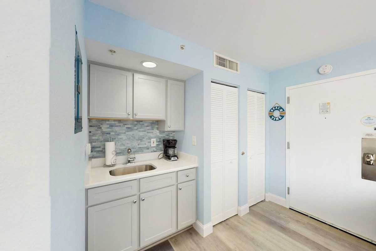 A compact kitchen with white cabinets, a sink, and a coffee maker.