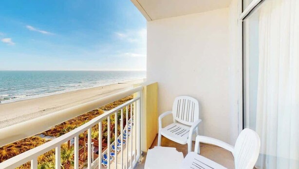 Ein Balkon mit Blick auf den Strand, weißen Stühlen und einer Glastür.
