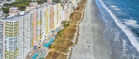 A coastal hotel with multiple floors, a beachfront, and a pool area.