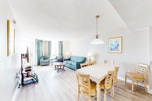 A spacious living area with a dining table, chairs, a sofa, and a TV stand. - Bay Watch Resort 0717 (North Myrtle Beach)