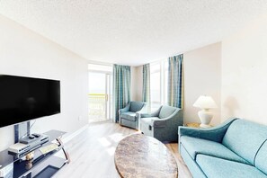 Ein modernes Wohnzimmer mit einem Flachbildfernseher, zwei Sesseln, einem Sofa, einem Couchtisch und einer Lampe.