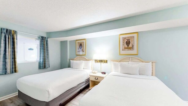 Een hotelkamer met twee bedden, een raam met gordijnen en een muur met ingelijste foto's.