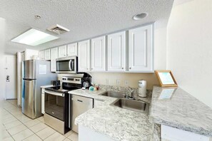 A modern kitchen with white cabinets, stainless steel appliances, a marble countertop, and a built-in microwave. - Bay Watch Resort 0714 (North Myrtle Beach)