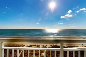 A beach view with a clear sky, a sun reflecting on the water, and a white railing in the foreground. - Bay Watch Resort 0714 (North Myrtle Beach)