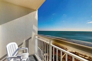 A balcony with a white chair, a railing, and a view of the beach and ocean. - Bay Watch Resort 0714 (North Myrtle Beach)