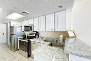 A modern kitchen with white cabinets, stainless steel appliances, a marble countertop, and a built-in microwave. - Bay Watch Resort 0714 (North Myrtle Beach)