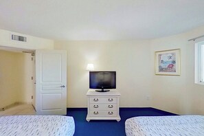 Ein Zimmer mit einem Bett, einem Schminktisch, einem Fernseher und einem gerahmten Bild an der Wand.