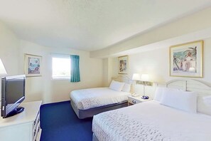 Ein Hotelzimmer mit zwei Betten, einem Fernseher, einem Schreibtisch und Bildern an der Wand.