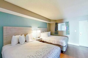 Ein Hotelzimmer mit zwei Betten, einem Nachttisch mit Lampe und einem Fenster mit Vorhängen.