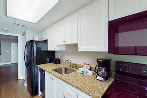 A kitchen with white cabinets, a black refrigerator, a granite countertop, a sink, a coffee maker, and a red stove.