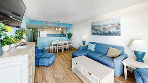 Ein modernes Wohnzimmer mit einem blauen Sofa, einem weißen Couchtisch und einem Essbereich mit Tisch und Stühlen.