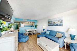 Ein modernes Wohnzimmer mit einem blauen Sofa, einem weißen Couchtisch und einem Essbereich mit Tisch und Stühlen.