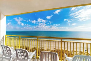 Ein Balkon mit Meerblick, ausgestattet mit weißen Plastikstühlen und einem gelben Geländer.