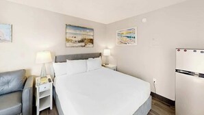 Ein Hotelzimmer mit einem Bett, Nachttischen, einer Lampe, einem Kühlschrank und Wandbildern.