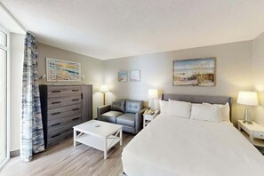 Ein Hotelzimmer mit einem Bett, einem Sofa, einem Schreibtisch und einer Kommode. An den Wänden hängen zwei Bilder und es gibt ein Fenster mit Vorhängen.
