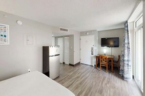 Hotelkamer met een bed, kitchenette, eethoek met tafel en stoelen, flatscreen televisie en raam met gordijnen.