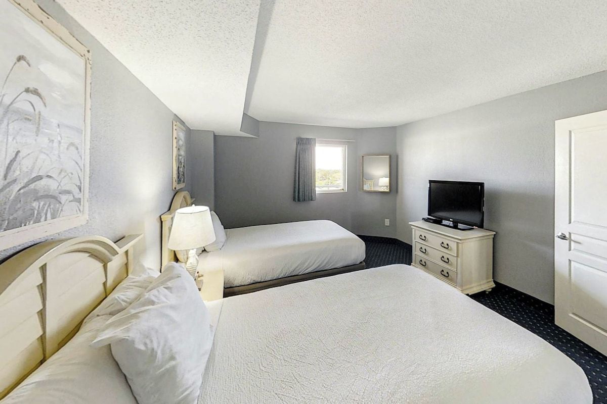 Une chambre d’hôtel avec deux lits, une télévision, une commode et une fenêtre avec des rideaux.