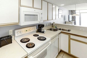 A kitchen with white cabinets, a microwave, a stove, a sink, and a window with curtains. - Bay Watch Resort 0814 (North Myrtle Beach)