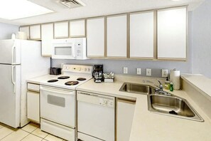 A kitchen with white appliances, a dishwasher, a sink, and cabinets above the countertop. - Bay Watch Resort 0814 (North Myrtle Beach)