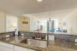 A modern kitchen with granite countertops, a stainless steel sink, and a hanging light fixture. - Bay Watch Resort 0817 (North Myrtle Beach)
