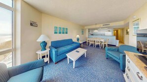 Ein Hotelzimmer mit einem blauen Sofa, einem weißen Couchtisch und einer Essecke mit Tisch und Stühlen.