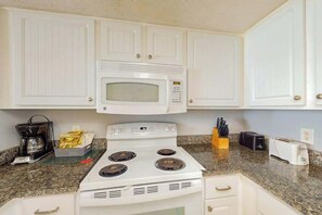 Eine Küche mit weißen Schränken, einer Mikrowelle, einem Herd, einer Kaffeemaschine, einem Toaster und einem Messerblock.