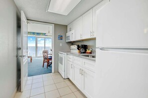 A compact kitchen with white cabinets, a microwave, a coffee maker, and a refrigerator. - Bay Watch Resort 0906 (North Myrtle Beach)