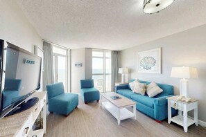 A hotel room with a television, a sofa, a coffee table, and a lamp. - Bay Watch Resort 0833 (North Myrtle Beach)