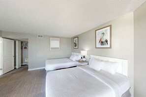 A hotel room with two beds, a bedside table with a lamp, and a door leading to a bathroom. - Bay Watch Resort 0833 (North Myrtle Beach)