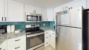 Eine Küche mit weißen Schränken, einem Edelstahlkühlschrank, einer Mikrowelle und einem Backofen.