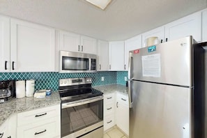 A kitchen with white cabinets, a stainless steel refrigerator, a microwave, and an oven. - Bay Watch Resort 0833 (North Myrtle Beach)
