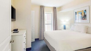 Una habitación de hotel con una cama, un escritorio con teléfono, un televisor montado en la pared y una ventana con cortinas.