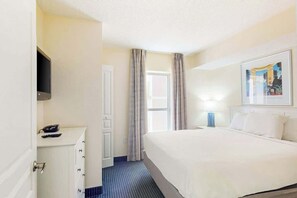 Ein Hotelzimmer mit einem Bett, einem Schreibtisch mit Telefon, einem an der Wand befestigten Fernseher und einem Fenster mit Vorhängen.