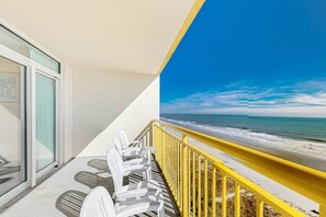 Ein Balkon mit Blick auf den Ozean, weiße Stühle und ein gelander.