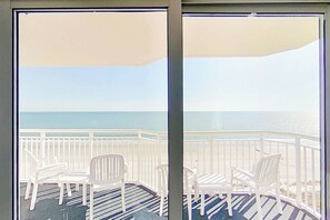 Un balcón con sillas blancas y piso a rayas, con vistas a una playa.