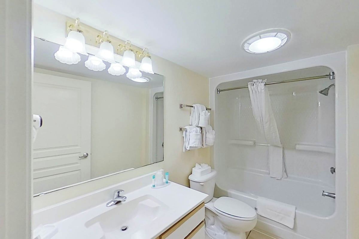 Une salle de bain équip ée d’un lavabo, d’un miroir, de toilettes et d’une douche.