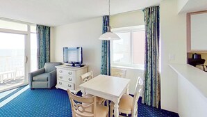 Een hotelkamer met een televisie, een eettafel, een bank en een raam met gordijnen.