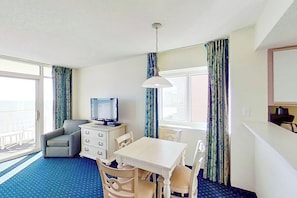 A hotel room with a television, a dining table, a sofa, and a window with curtains. - Bay Watch Resort 0922 (North Myrtle Beach)