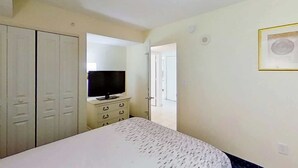 Een slaapkamer met een bed, een televisie op een dressoir en een kledingkast.