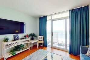 Ein Wohnzimmer mit Flachbildfernseher, einem kleinen Tisch mit Topfpflanze, einem Sessel und einer Couch.
