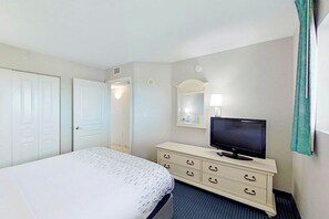 A hotel room with a bed, a dresser with a television, a mirror, and a door. - Bay Watch Resort 1037 (North Myrtle Beach)