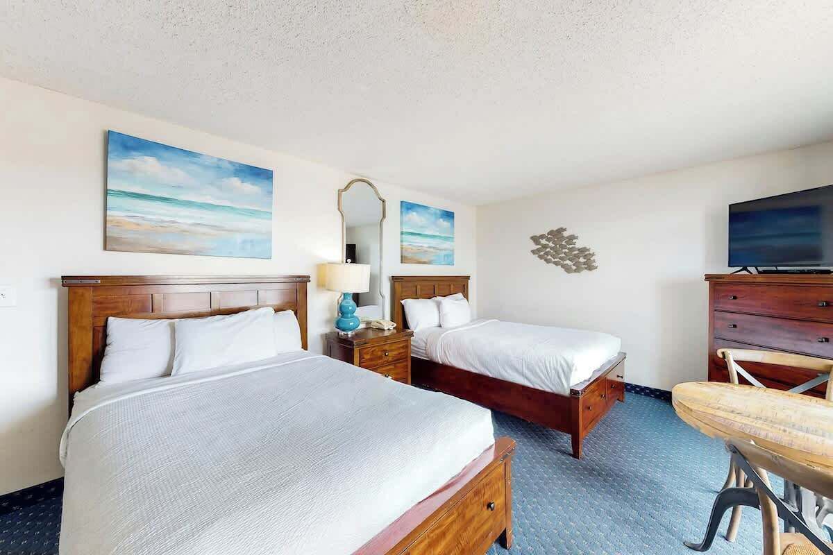 Ein Hotelzimmer mit zwei Betten, einem Schreibtisch mit Stuhl, einem Fernseher und Bildern an den Wänden.