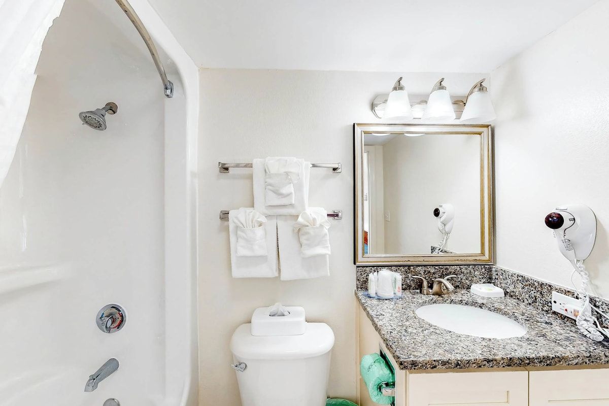 A bathroom with a shower, toilet, sink, and a towel rack with towels.